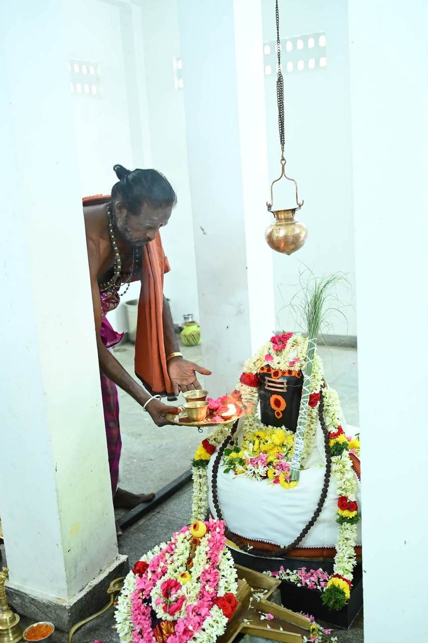 Priest performing abhishekam to a flower-adorned Shiva lingam
