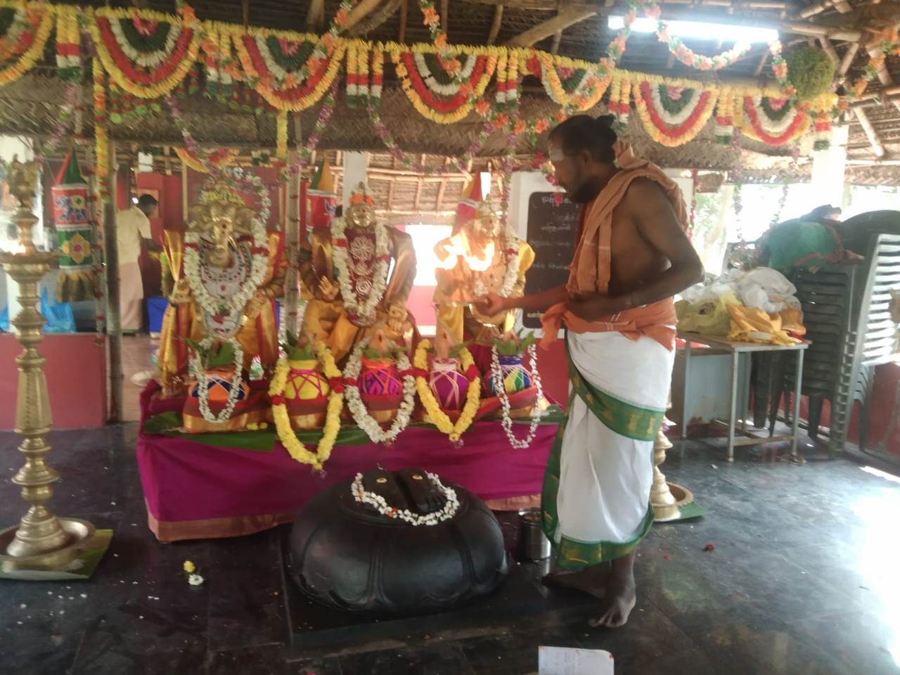 Priest performing pooja before golden deities
